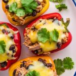 Stuffed bell peppers with turkey and black beans on a plate, topped with melted cheese and garnished with cilantro.